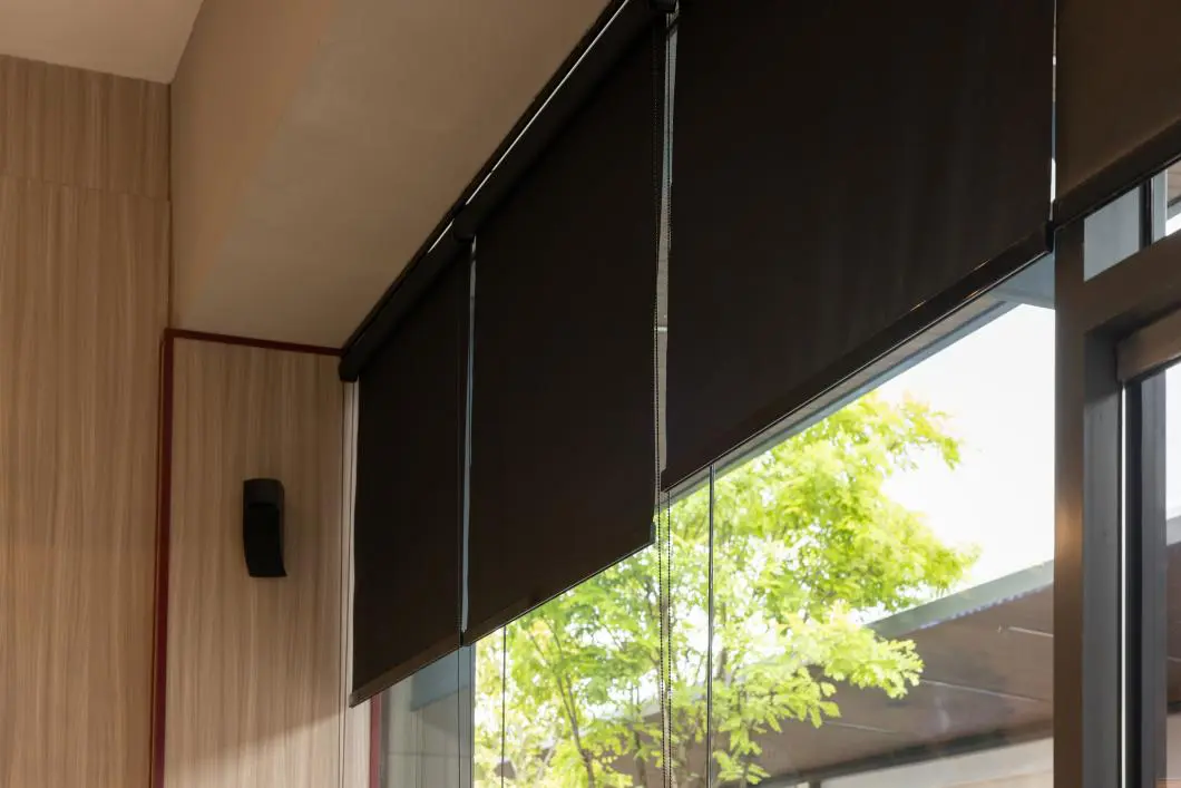 GettyImages-2159941275 Black window blinds with trees outside view.