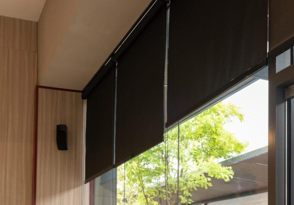 Black window blinds with trees outside view.